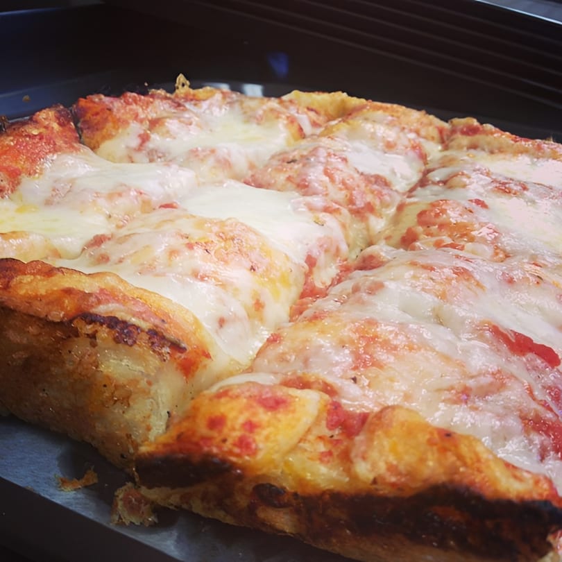 Close-up of a thick-crust square pizza from Cosmo's, topped with melted cheese and tomato sauce.