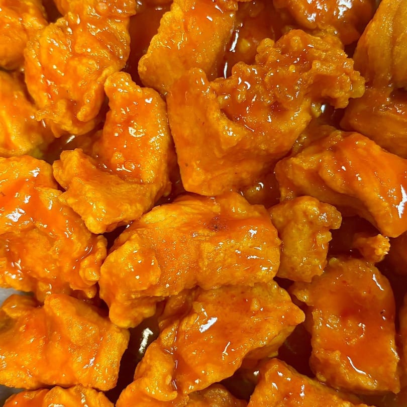 Close-up of Cosmo's boneless chicken wings coated in a vibrant orange sauce.