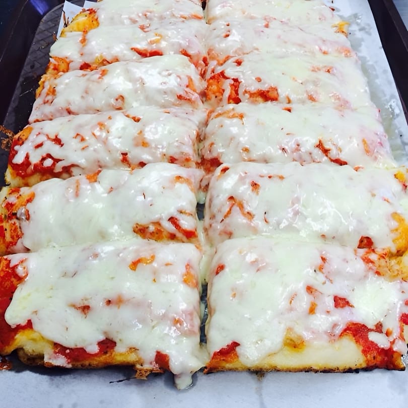 Rows of Cosmo's cheesesteak pizza slices with melted white cheese and red sauce.