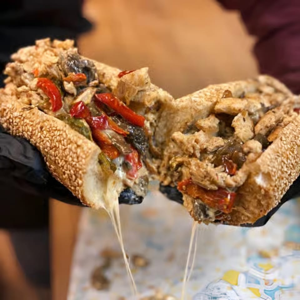 Hands in black gloves holding a Cosmo's cheesesteak, split open with melted cheese stretching.