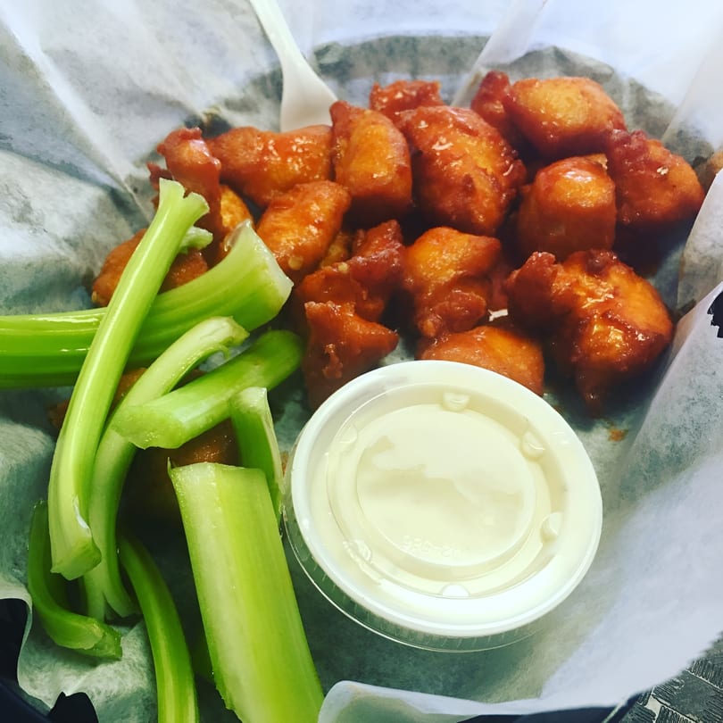 Cosmo's boneless wings with celery sticks and a side of ranch dressing in a basket.